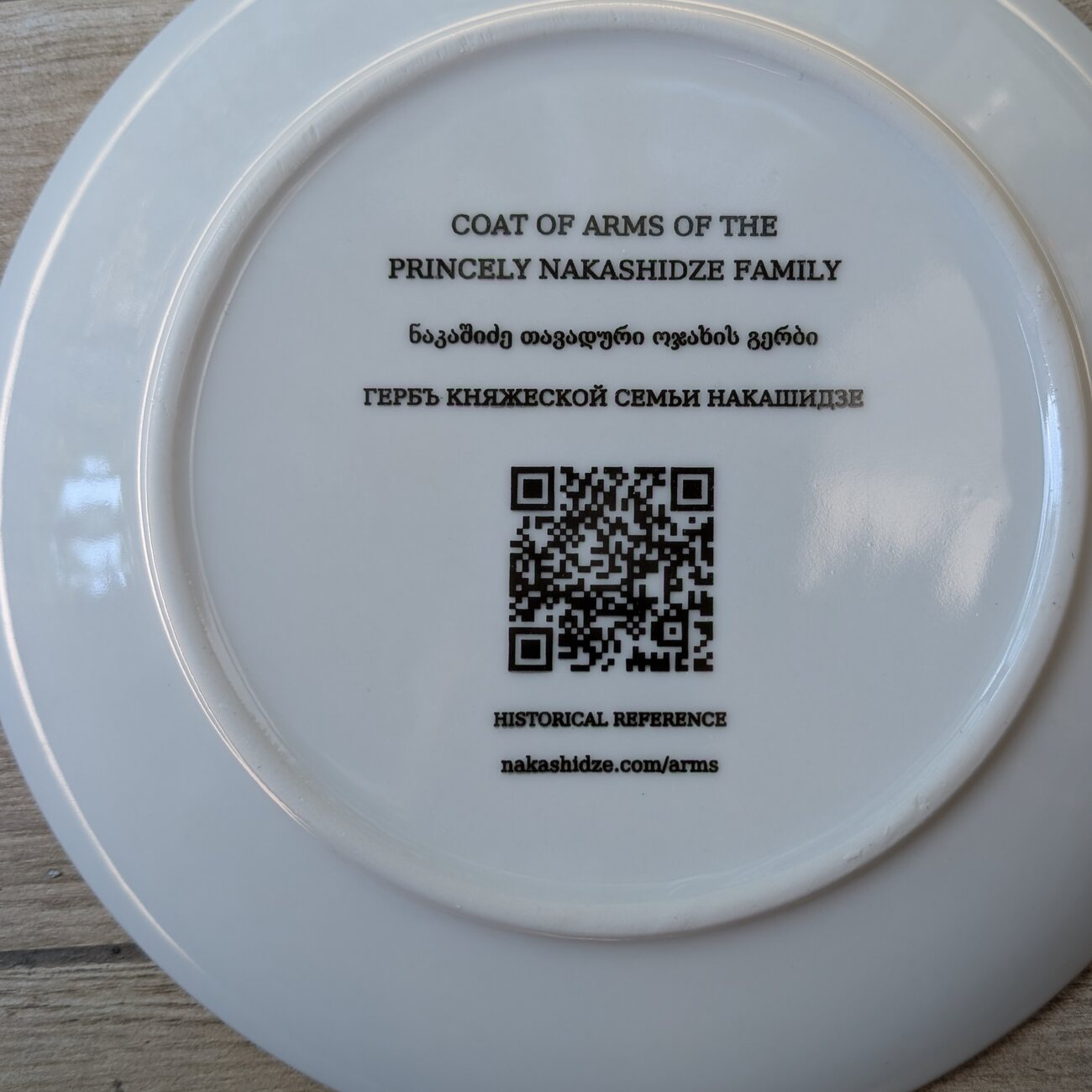 The reverse of the Nakashidze commemorative plate, printed with the title in English, Georgian and Russian, a QR code, and the address nakashidze.com/arms.