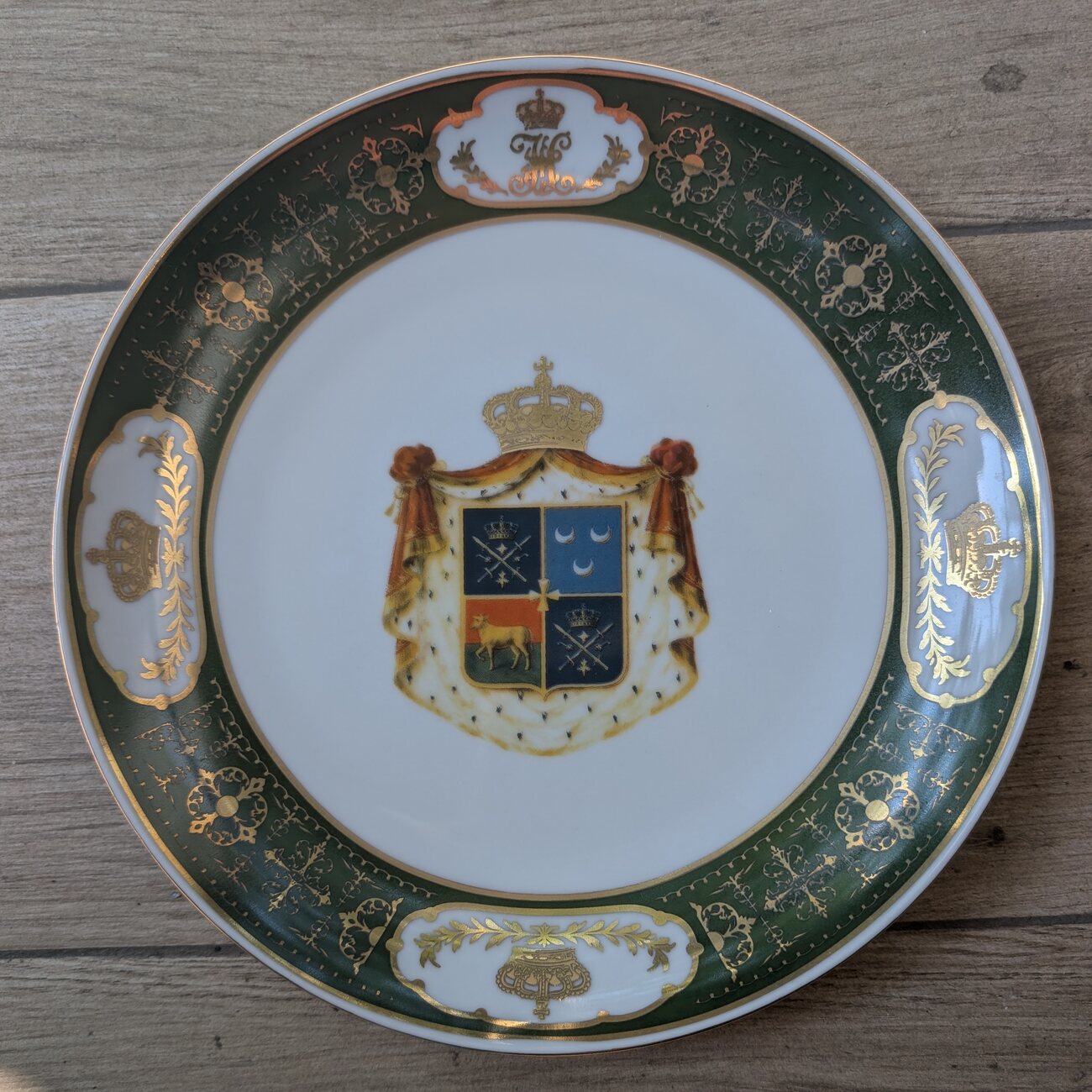 Photograph of the Nakashidze commemorative plate — a deep-green and gold porcelain rim framing the family coat of arms at its centre.